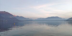 Lac d’Annecy bleu-gris au crépuscule sous une lune claire.