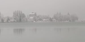 Le lac d’Annecy gris et brumeux devant une rive enneigée.
