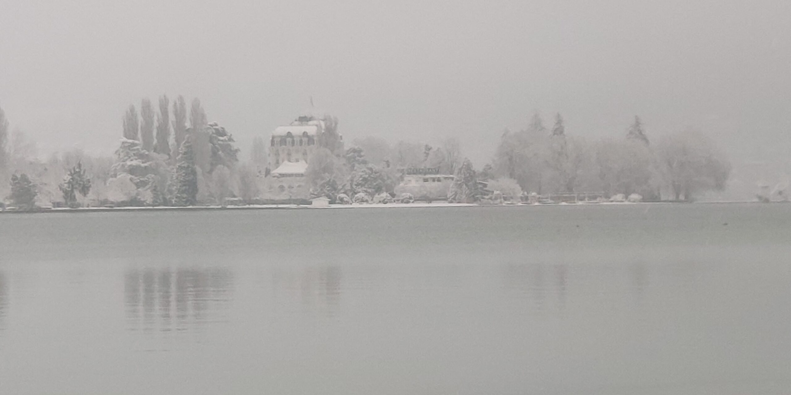 Le lac d’Annecy gris et brumeux devant une rive enneigée.