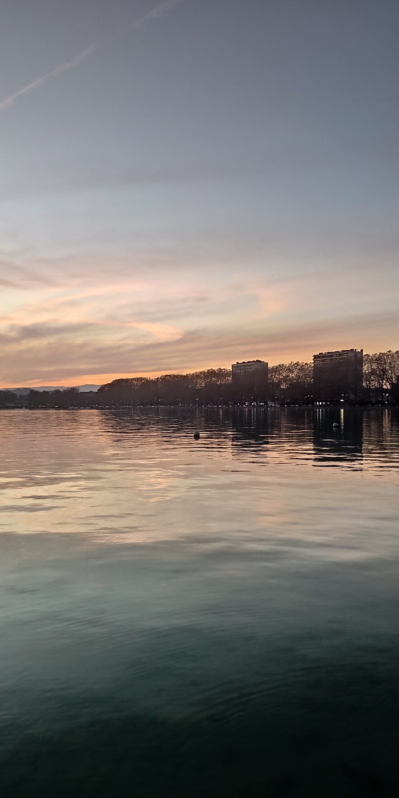 Reflets roses et argentés sur le lac devant la ville d’Annecy.